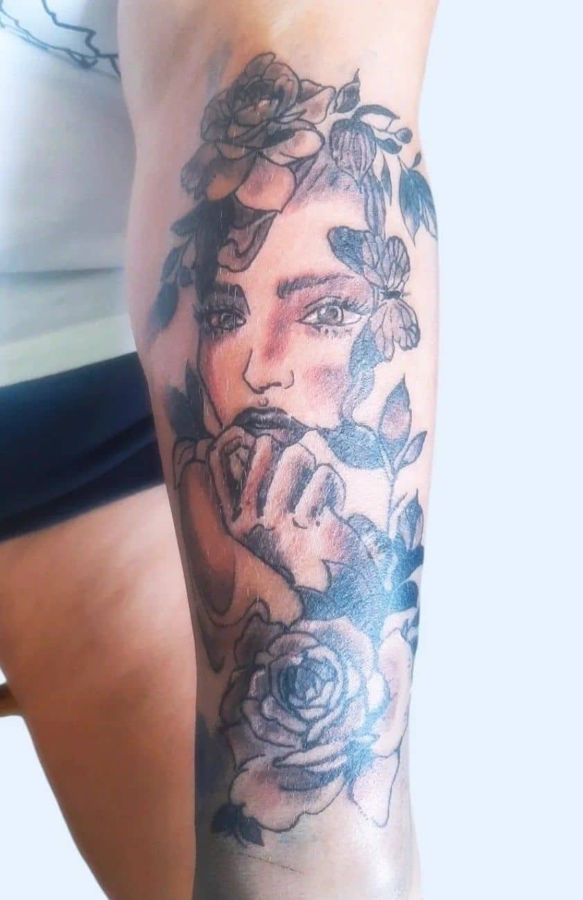 Tattoo by Jake Brewer, woman's face among roses on a forearm