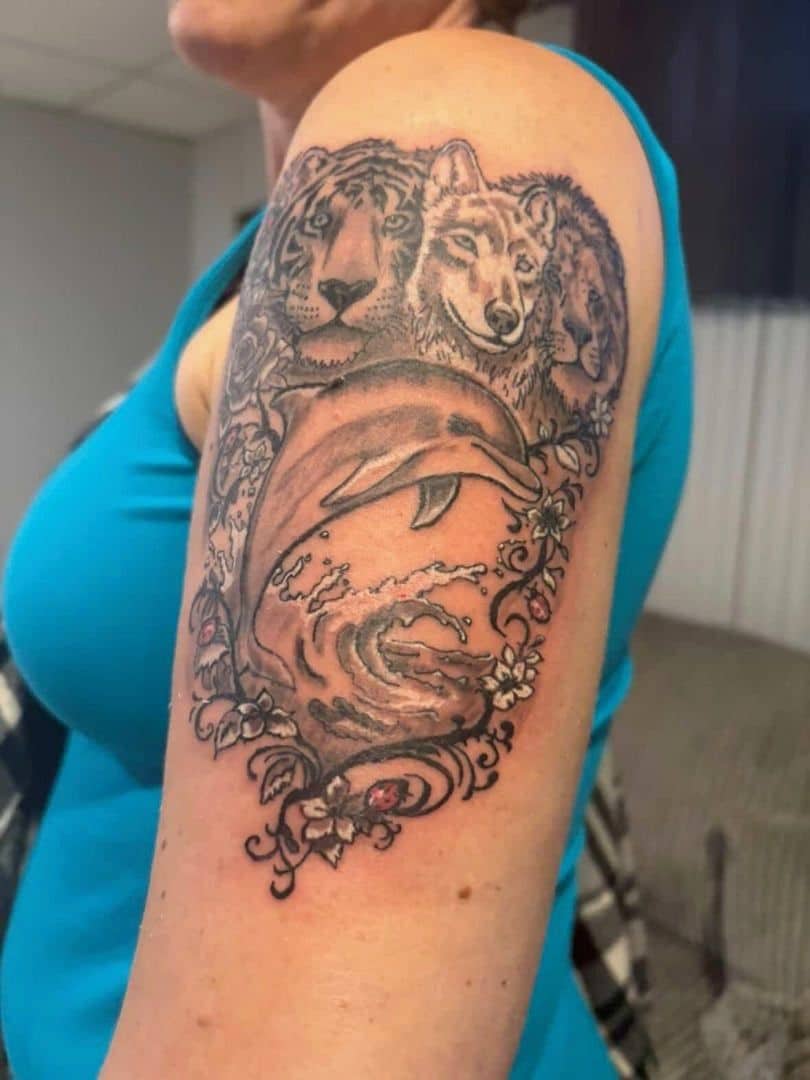 Tattoo by Jake Brewer, tiger and wolf above a dolphin riding a wave, on an upper arm