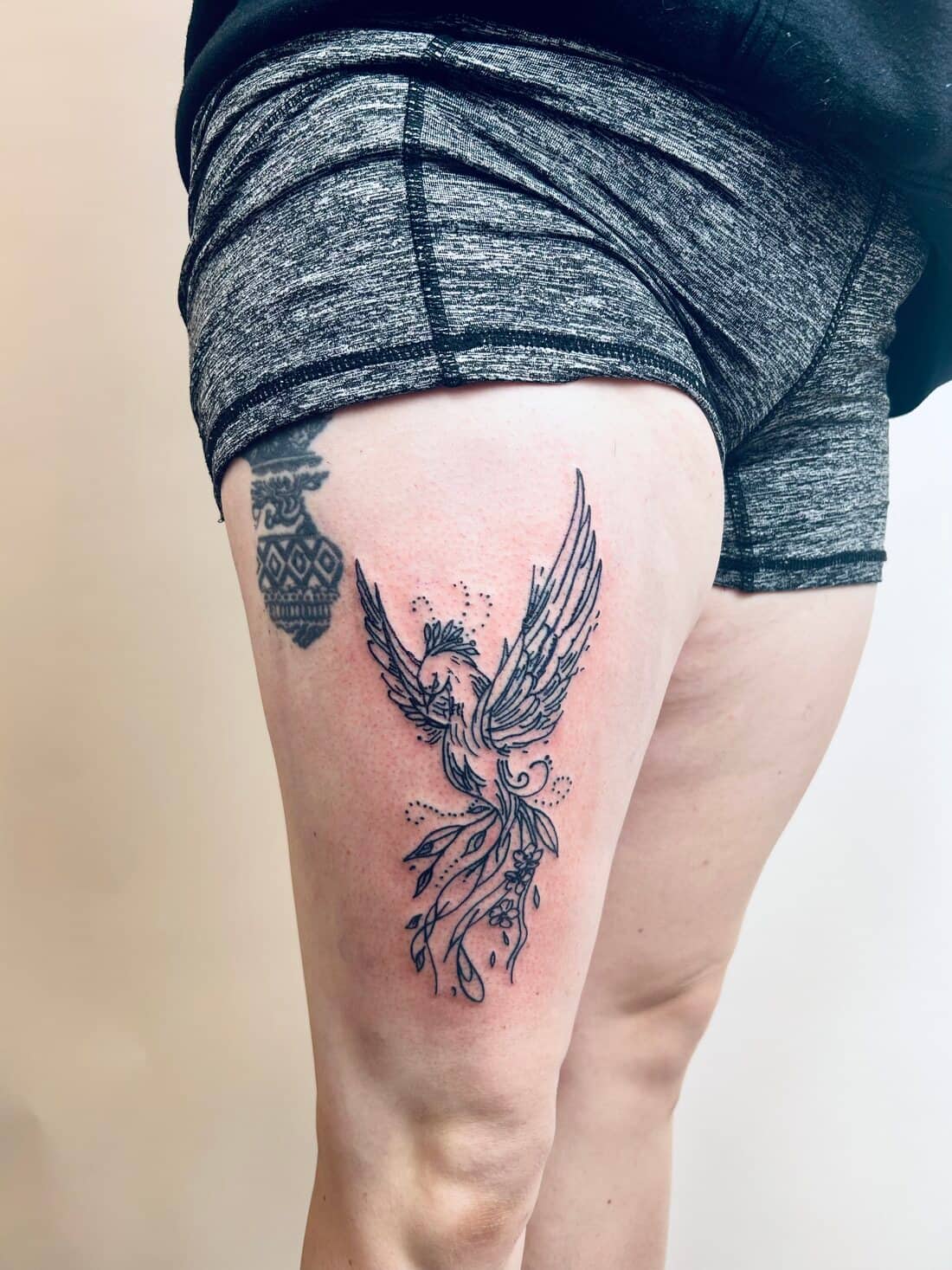 Tattoo by Apollonia Ink in Barrie, fine line phoenix with a botanical tail on a thigh
