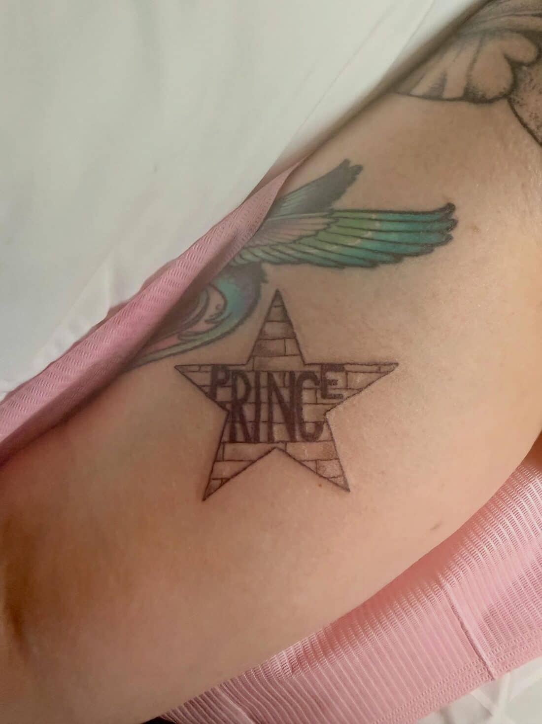 Tattoo by Apollonia Ink in Barrie, star with Prince lettering beside a blue and green wing