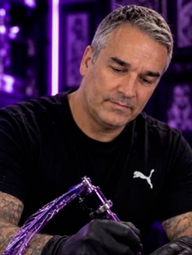 Ricardo Mendes tattooing a client, holding a purple machine